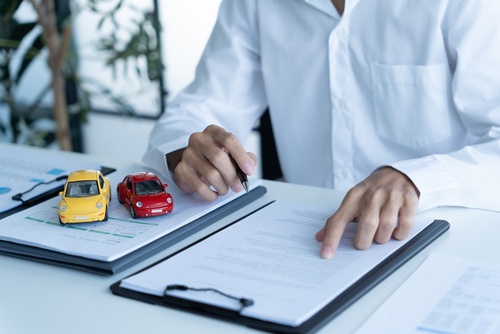 person holding pen over insurance documents with two toy cars on desk