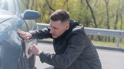 Man Inspecting Car Accident Damage Dayton Ohio man crouching beside vehicle closely inspecting body panel damage on roadside