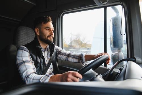 Commercial Truck Driver Behind the Wheel Fort Lauderdale young male truck driver seated in semi-truck cab gripping steering wheel