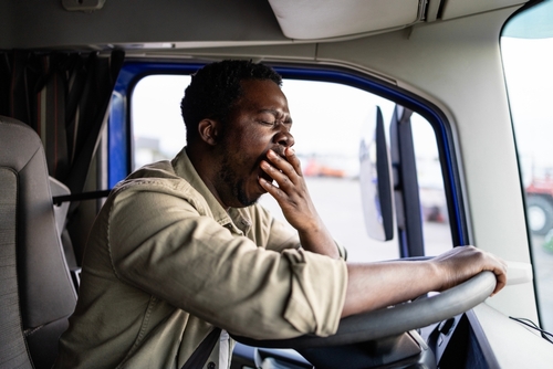 fatigued truck driver yawning while seated behind steering wheel in cab