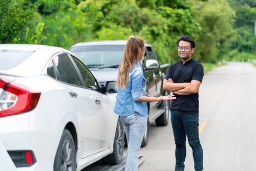 two people arguing roadside near damaged vehicles after car accident
