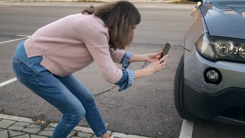 Woman Photographing Car Damage After Cincinnati Crash woman crouching to photograph vehicle front end damage with smartphone