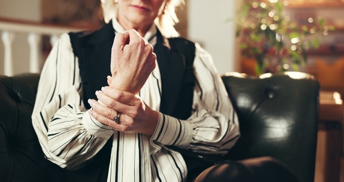 older woman clutching wrist in pain while seated in leather chair