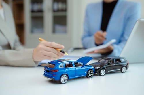 Philadelphia Commercial Fleet Accident Insurance Claim Signing person signing document beside two toy cars depicting collision on desk