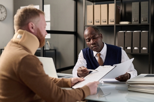 Philadelphia Workers Comp Lawyer Reviewing Denied PA Claim professional advisor reviewing documents with neck-brace-wearing client across office desk