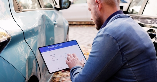 Man Filing Commercial Auto Insurance Claim Trenton NJ man filing Insurance Claim form on tablet beside damaged vehicle