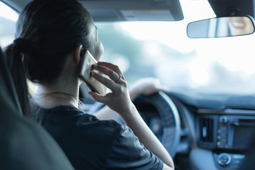 driver holding smartphone to ear while gripping steering wheel in vehicle