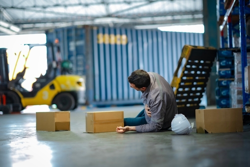 Philadelphia Slip and Fall Injury in Warehouse injured warehouse worker sitting on floor beside cardboard boxes and hard hat