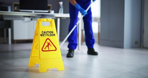 Caution Wet Floor sign beside janitor mopping indoor floor with mop