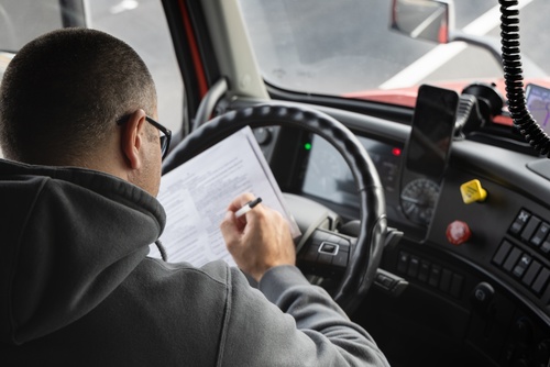 Truck Driver Reviewing Logbook Inside Cab Fort Lauderdale truck driver seated in cab reviewing and signing document with pen