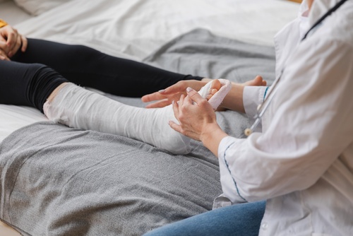 doctor in white coat examining patient leg wrapped in plaster cast