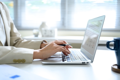office professional typing on laptop while holding pen at desk