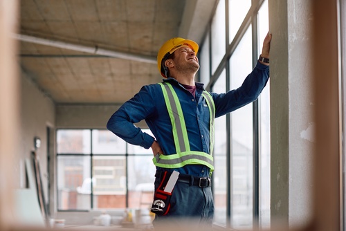 construction worker in hard hat and safety vest grimacing from lower back pain