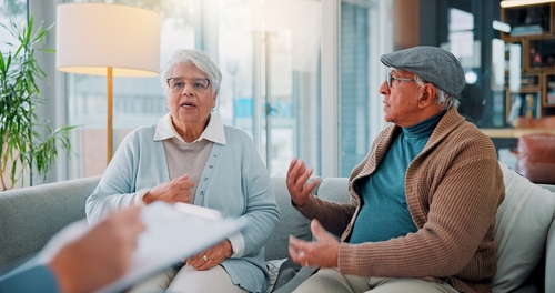 Senior Couple Discussing Pension Division During Las Vegas Divorce elderly couple seated on sofa speaking with professional holding clipboard