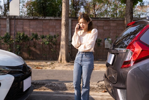 distressed woman on phone call standing between two vehicles after collision