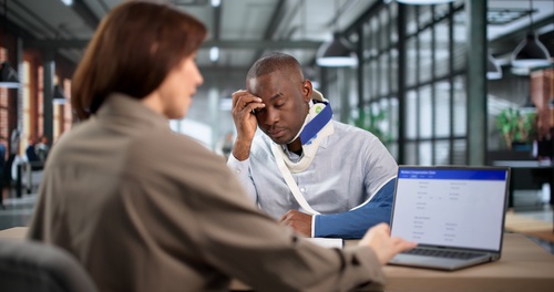 Philadelphia Commercial Auto Accident Lawyer Helping Injured Client injured man wearing neck brace and arm sling meeting with attorney reviewing laptop