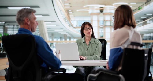professional woman with laptop consulting two wheelchair-using clients in modern office