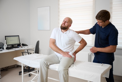 Chicago Car Accident Injury Treatment Before Settlement man gripping hip in pain while medical professional examines him in clinic