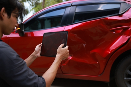 person holding tablet photographing dented car door after vehicle collision