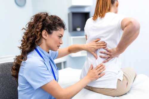 BWC Certified Doctor Treating Dayton Work Injury Patient female healthcare professional examining seated patient's lower back in clinical setting