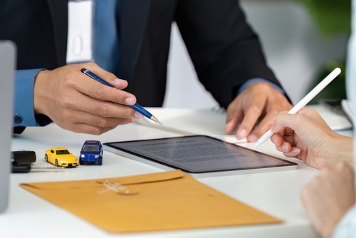 Sacramento Car Insurance Policy Consultation After Accident two people reviewing document on tablet with toy cars and envelope on desk