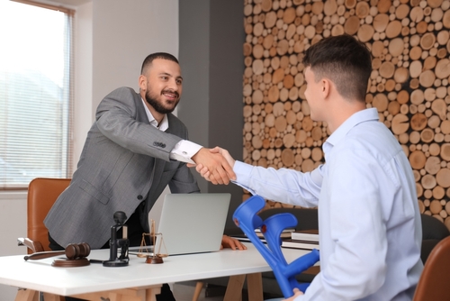 attorney shaking hands with injured client holding crutches across office desk