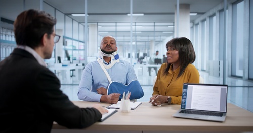 Centennial Truck Accident Lawyer Consulting Injured Client injured man wearing neck brace and arm sling meets with attorney at office desk