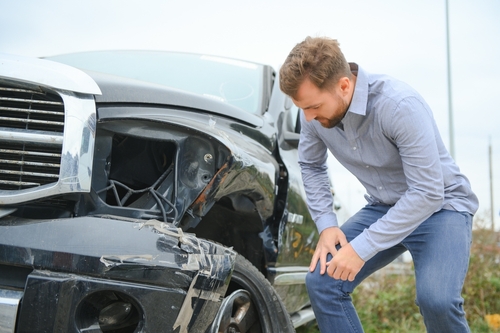 man hunched over in pain beside severely damaged vehicle after car accident