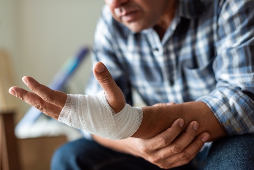 person in plaid shirt holding bandaged hand and wrist injury