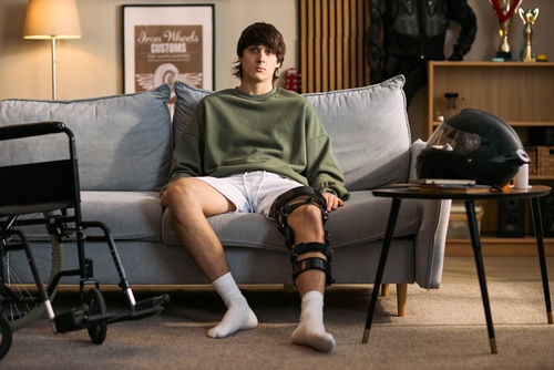teenage male seated on couch wearing knee brace with wheelchair nearby