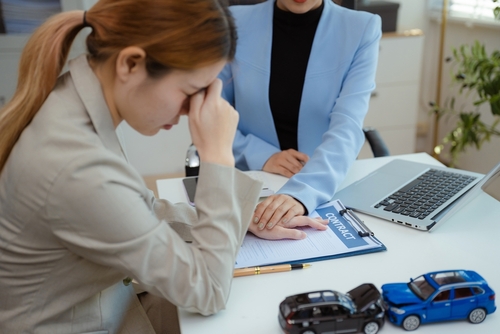 Indianapolis Car Accident Fault Based Insurance Claim Meeting distressed woman reviewing insurance contract document with toy car collision models on desk