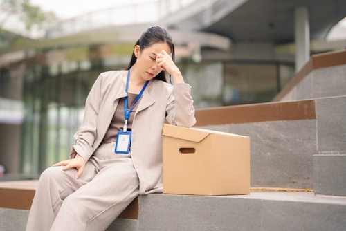distressed professional woman wearing ID badge sitting outdoors beside cardboard box