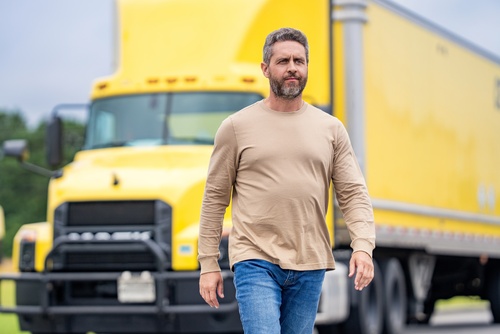 male truck driver walking in front of large commercial semi-trucks