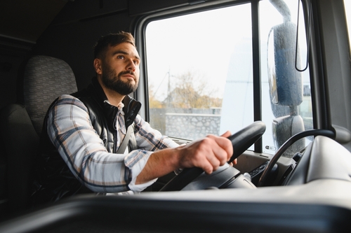 Commercial Truck Driver Behind the Wheel in Houston Texas bearded male truck driver gripping steering wheel inside commercial truck cab