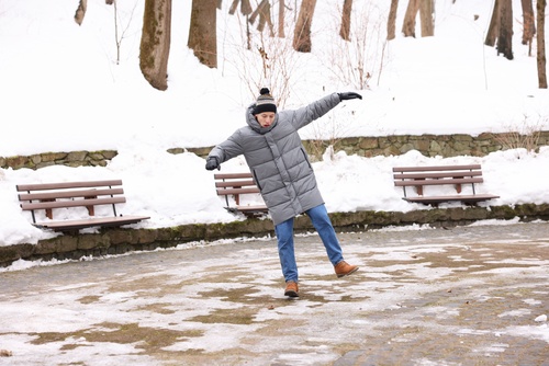 man slipping on icy pavement in snow-covered park with benches