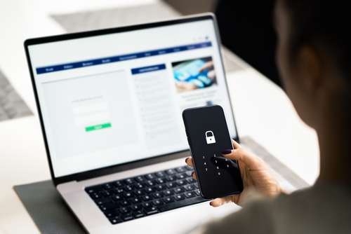 Investor Protecting Account From Securities Fraud USA person holding smartphone displaying lock icon and numeric passcode screen near laptop