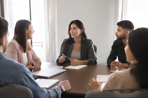 professional woman leading discussion with colleagues seated around conference table