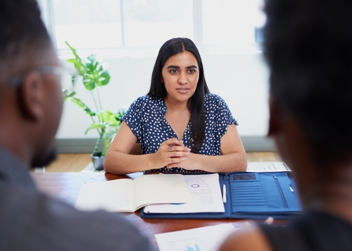 female mediator speaking with clients across conference table with documents