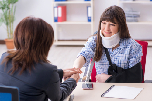 injured woman wearing neck brace and arm sling meeting with attorney in office