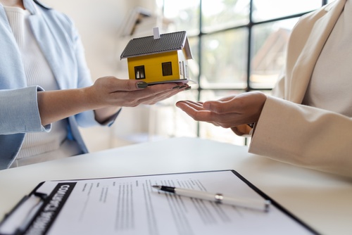Houston Homeowner Reviewing Denied Home Insurance Claim two people exchanging miniature house model over signed legal contract document