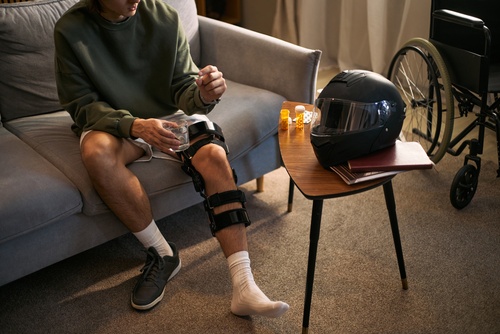 Injured Morgantown Motorcycle Rider Recovering After Left Turn Crash injured man wearing knee brace seated on couch with motorcycle helmet and wheelchair nearby
