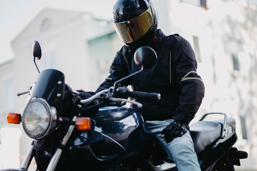 male motorcyclist wearing full-face helmet and jacket seated on motorcycle