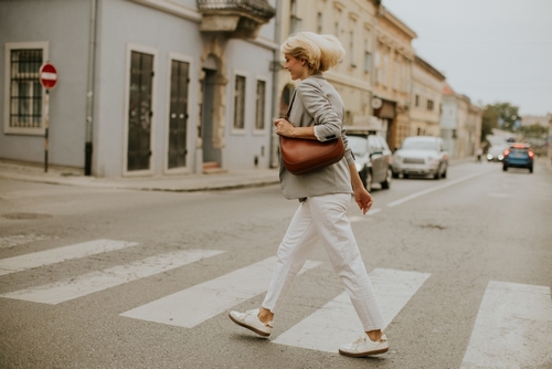 woman carrying shoulder bag walking across marked pedestrian crosswalk on urban street