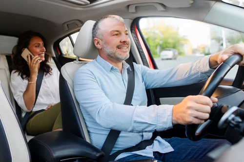 male driver gripping steering wheel while female passenger talks on cellphone