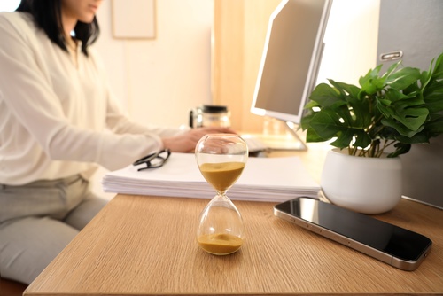 Illinois Car Accident Claim Deadline Hourglass hourglass and mobile phone on desk with woman working at computer