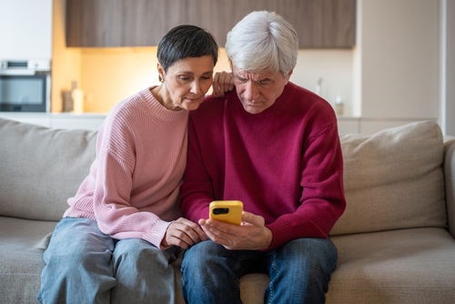 Elderly Couple Victims of Online Scam Los Angeles elderly couple seated on sofa together reviewing content on smartphone