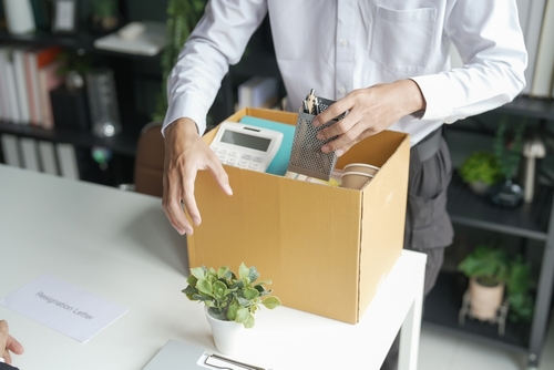 employee packing personal belongings into cardboard box beside resignation letter