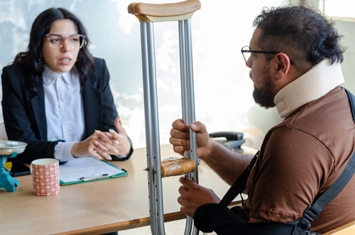 Philadelphia Car Accident Lawyer Consulting Injured Crash Victim female attorney consulting injured client wearing neck brace holding crutches at desk