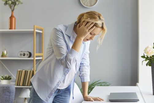 Woman With Head Pain After Traumatic Brain Injury Fort Worth stressed woman leaning over desk holding head with hand near laptop