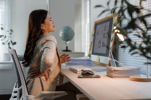 office worker seated at desk clutching lower back in discomfort